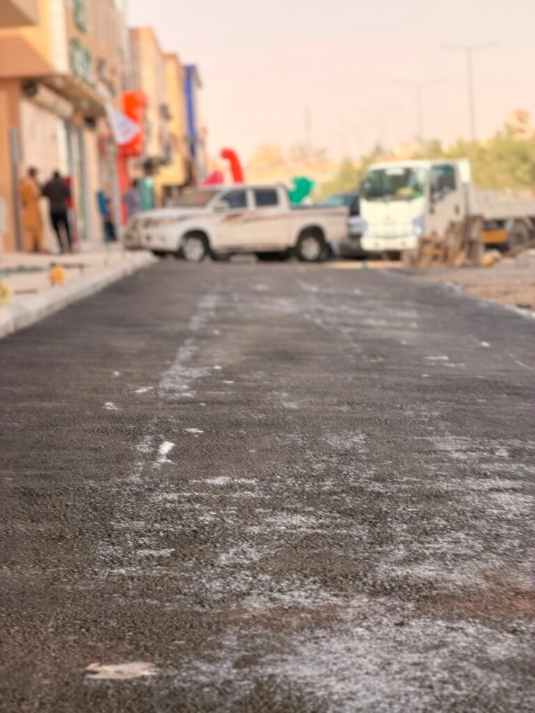 سطح أسفلت ممهد بجانب تربة حمراء في موقع سفلتة بالمزاحمية